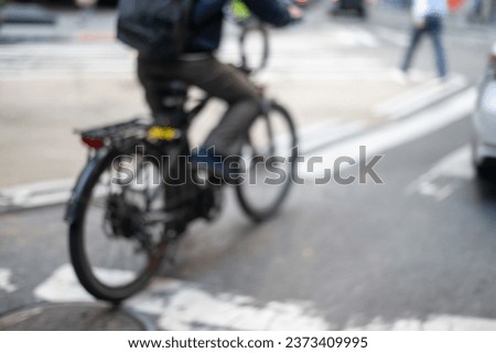 Abstract defocused background bike rider in urban city street with asphalt markings, crosswalks, sidewalk, cars and pedestrians.