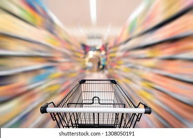 Abstract Defocused Blurred Of Consumer Goods And Shopping Cart In Supermarket Store, Shop Trolley Basket In Department Store. Business Retail And Customer Shopping Mall Service, Motion Blurry Concept.