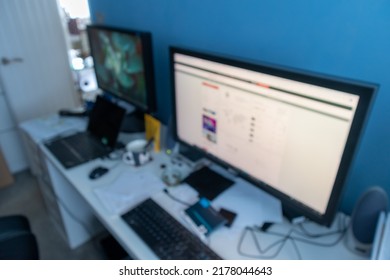 Abstract De-focused Image Of A Working From Home Office Featuring A White Desk With Two Screens And Blue Feature Wall