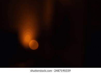 Abstract defocused warm light source in a dark room, creating a moody and atmospheric effect. The soft orange glow contrasts with the deep shadows, suggesting a calm and serene ambiance.