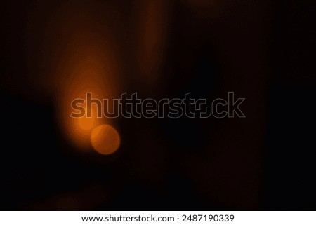Abstract defocused warm light source in a dark room, creating a moody and atmospheric effect. The soft orange glow contrasts with the deep shadows, suggesting a calm and serene ambiance.