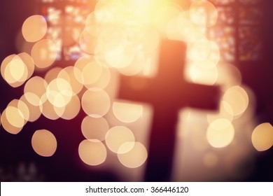 Abstract defocussed cross silhouette in church interior against stained glass window concept for religion and prayer