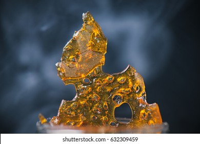 Abstract detail of cannabis oil concentrate aka shatter with smoke over dark background