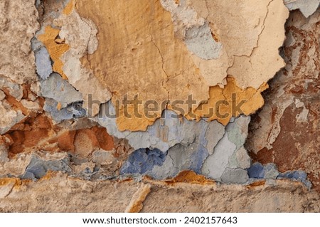 Abstract, detail, pattern of a section of multi-colored, blue, ochre, yellow and brown peeling paint layers on an old stone exterior wall of a residence in Jerusalem, Israel.