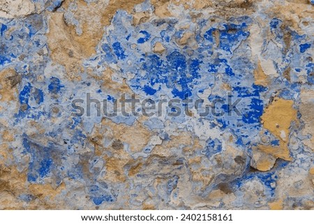 Abstract, detail, pattern of a section of multi-colored, peeling blue and yellow paint layers on an old stone exterior wall of a residence in Jerusalem, Israel.