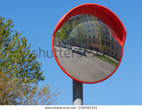 Abstract distorted image of urban landscape\
and cars in orange round frame. Reflection in spherical mirror on\
blurry background of sky and tree. Concept of road safety. Focus on\
foreground.\
