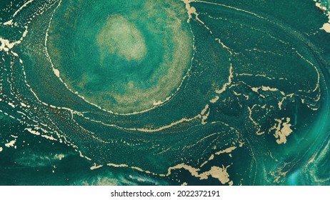 Abstract Explosion Of Green Paints Gold Sparkles Close-up. Hypnotic Current Liquid Ink. Emerald Color Of Spreading, Moving Mesmerizing Background. Texture Of Golden Threads On Green Tide