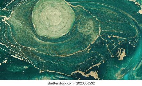 Abstract Explosion Of Green Paints Gold Sparkles Close-up. Hypnotic Current Liquid Ink. Emerald Color Of Spreading, Moving Mesmerizing Background. Texture Of Golden Threads On Green Tide