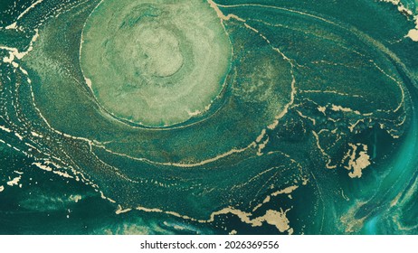 Abstract Explosion Of Green Paints Gold Sparkles Close-up. Hypnotic Current Liquid Ink. Emerald Color Of Spreading, Moving Mesmerizing Background. Texture Of Golden Threads On Green Tide