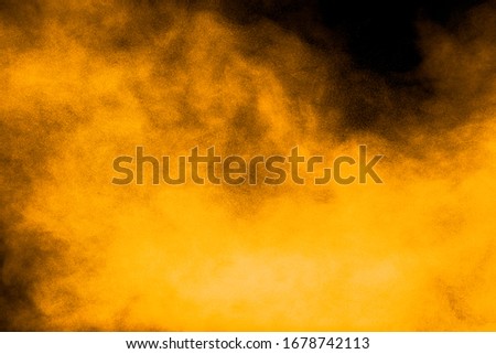 Abstract explosion of orange dust on black background. Freeze motion of orange powder burst.