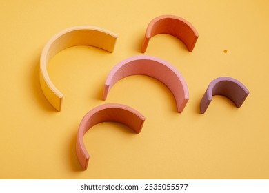 Abstract figures from elements of the children's designer wooden pastel rainbow on a wooden podium on a paper background. 