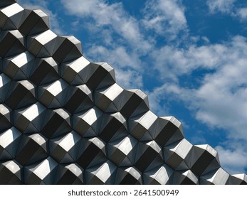 Abstract geometric architecture with metallic hexagonal patterns against a blue sky with scattered clouds.