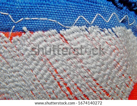 Abstract grunge blue red background fabric flag quilted with white thread.The texture of the darning threads.Decorative textile wallpaper design.