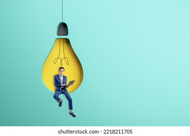 Abstract Image Of Attractive Young European Businessman Sitting On Abstract Hanging Light Bulb Chair And Using Laptop On Blue Background With Mock Up Place. 