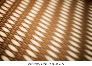 Abstract image featuring light and shadow patterns formed by a perforated surface, creating elongated oval shapes on a textured background