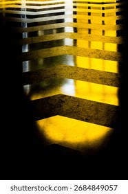 An abstract image featuring a pattern of yellow and black stripes, possibly a floor marking or a design element, with strong contrast and a play of light and shadow.