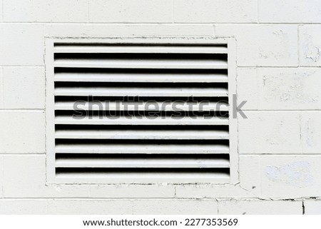 An abstract image of a large square air intake vent on a white exterior brick wall.  