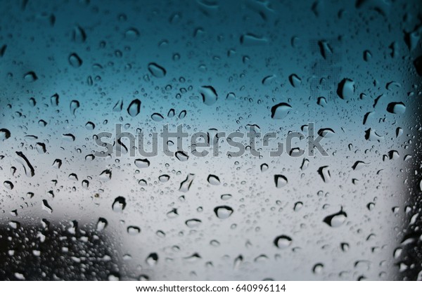 abstract image of rain drops on car window\
focusing on the rain droplets with blue\
sky