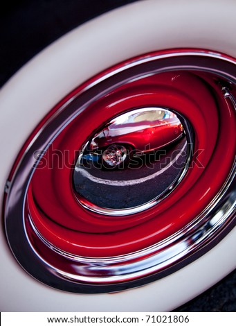 Abstract image of a vintage chrome wheel showing a distorted reflection of a portion of a vintage car.
