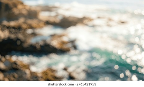 Abstract, impressionistic view of ocean waves meeting a rocky coast, with shimmering sunlight reflecting on the water's surface.