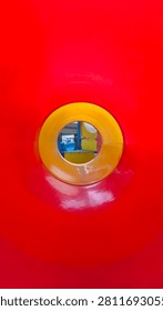 Abstract interior perspective of a bright red plastic playground tunnel with a yellow circular exit framing the background.