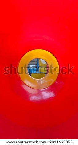 Abstract interior perspective of a bright red plastic playground tunnel with a yellow circular exit framing the background.