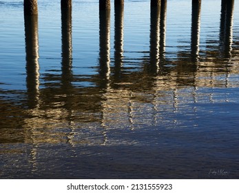 Abstract of jetty piers and reflection on the blue smooth water. Vertical lines and diagonal lines. Early morning sun hitting the pylons