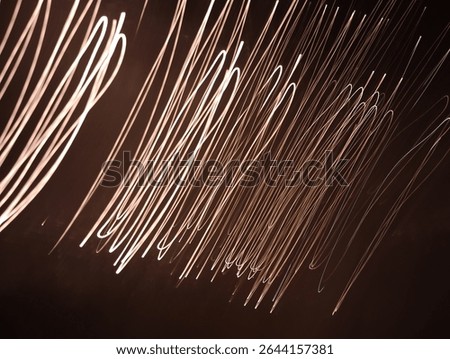 Abstract light trails captured using long exposure technique. Thin curved lines of white and orange glow streak across a dark background, creating an artistic sense of motion and energy. Perfect for t