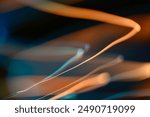 An abstract long exposure photograph showcasing fluid and colorful light trails against a dark background. The image features dynamic streaks of orange, blue, and teal, creating a mesmerizing