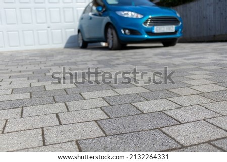 Abstract low angle blurred image of a blue car parked in a residential grey blockwork driveway