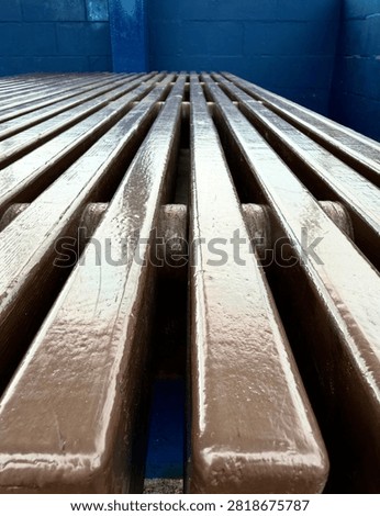 Abstract low angle perspective close up of brown slatted wooden bench, geometric pattern with leading lines against blue wall