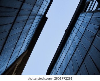 Abstract low angle view looking up between two modern building facades with a vertical panel pattern against a clear sky.
