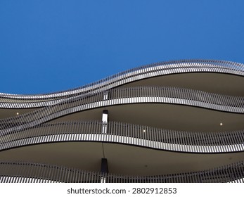 Abstract low angle view of a modern residential building facade with wavy curved balconies and metal railings against a clear blue sky.