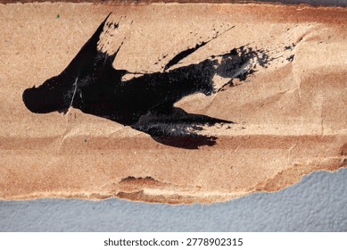 Abstract macro background featuring expressive black paint splatter on torn cardboard with natural paper texture and artistic grunge detail.