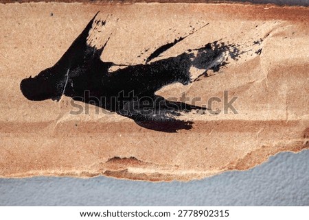Abstract macro background featuring expressive black paint splatter on torn cardboard with natural paper texture and artistic grunge detail.