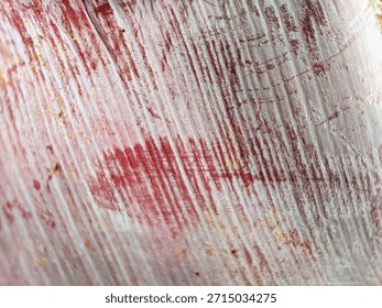 Abstract macro texture of weathered red painted wood with distressed white peeling layers. Gritty rustic background featuring organic scratches and vintage industrial erosion for creative design.