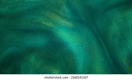 Abstract magic green background with golden sparkles. Photo of a green liquid with gold glitters. Various shades of green with golden splashes. Green backdrop with tints of golden glitters.