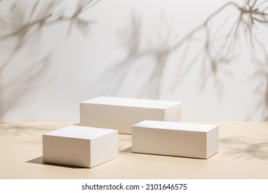 Abstract minimal nature scene - empty stage with three white rectangle podiums on beige background and shadows of pine tree. Pedestal for cosmetic product and packaging mockups display presentation - Shutterstock ID 2101646575