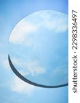 Abstract minimal scene with round mirror placed on blue background. The mirror reflects the clear blue sky and white clouds. Copy space