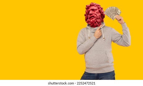 Abstract modern collage. The man with the plaster head of David Joyful man in a gray hoodie points a finger at money dollars on a yellow background - Shutterstock ID 2252472521
