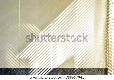 Abstract of morning light and shadow on tiled wall through window blind shutter. Parallel lines of light and reflection provide interesting abstract interior character. Light through blinds window.