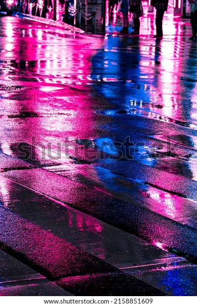 Abstract Neon\
light reflection at nightlife district from wet street with vehicle\
traffic and pedestrian walking by. Nightlife, futuristic metaverse\
city, and cyberpunk\
concept.