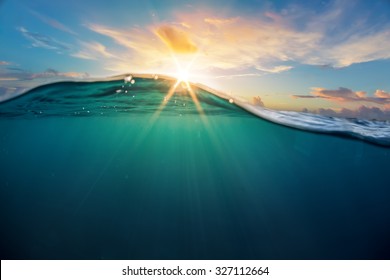 Abstract ocean design template with underwater part and sunset skylight splitted by waterline. Beautiful clouds and bright sun over sea water.