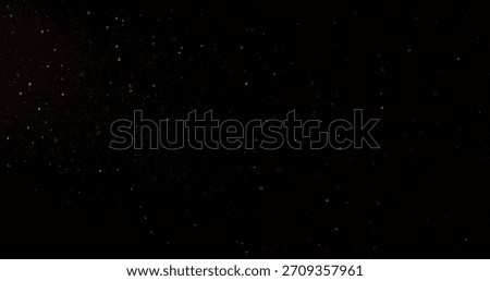 Abstract particles of gold dust float in the air, isolated against a black background with a warm yellow glow, creating a dreamy and cinematic atmosphere.