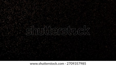 Abstract particles of gold dust float in the air, isolated against a black background with a warm yellow glow, creating a dreamy and cinematic atmosphere.