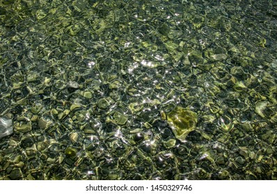 Abstract pattern of pebbles under the surface of the water. Background of shiny pebbles on the river bottom.