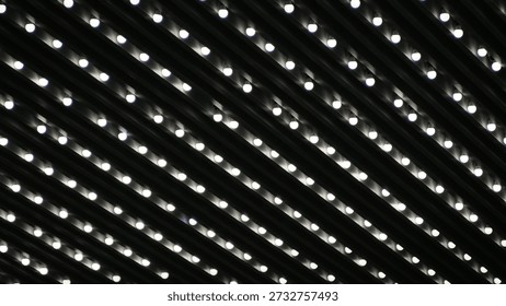 Abstract pattern of rows of glowing white light bulbs installed on a dark, slatted ceiling, creating a rhythmic and modern geometric aesthetic.