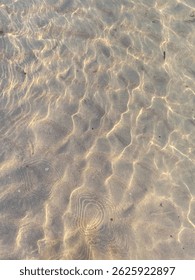 Abstract pattern of sunlight reflecting on clear, shallow sea water over sand. Natural light refractions creating a peaceful and minimal aquatic texture.