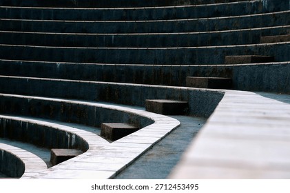 An abstract pattern of tiered circular steps or tribunes, consisting of light square stone tiles separated by dark gaps, with a green grass background to the side.