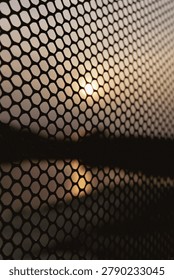 An abstract perspective of a wire mesh screen fence forming a silhouette grid pattern over the setting sun at Shangumugham Beach.